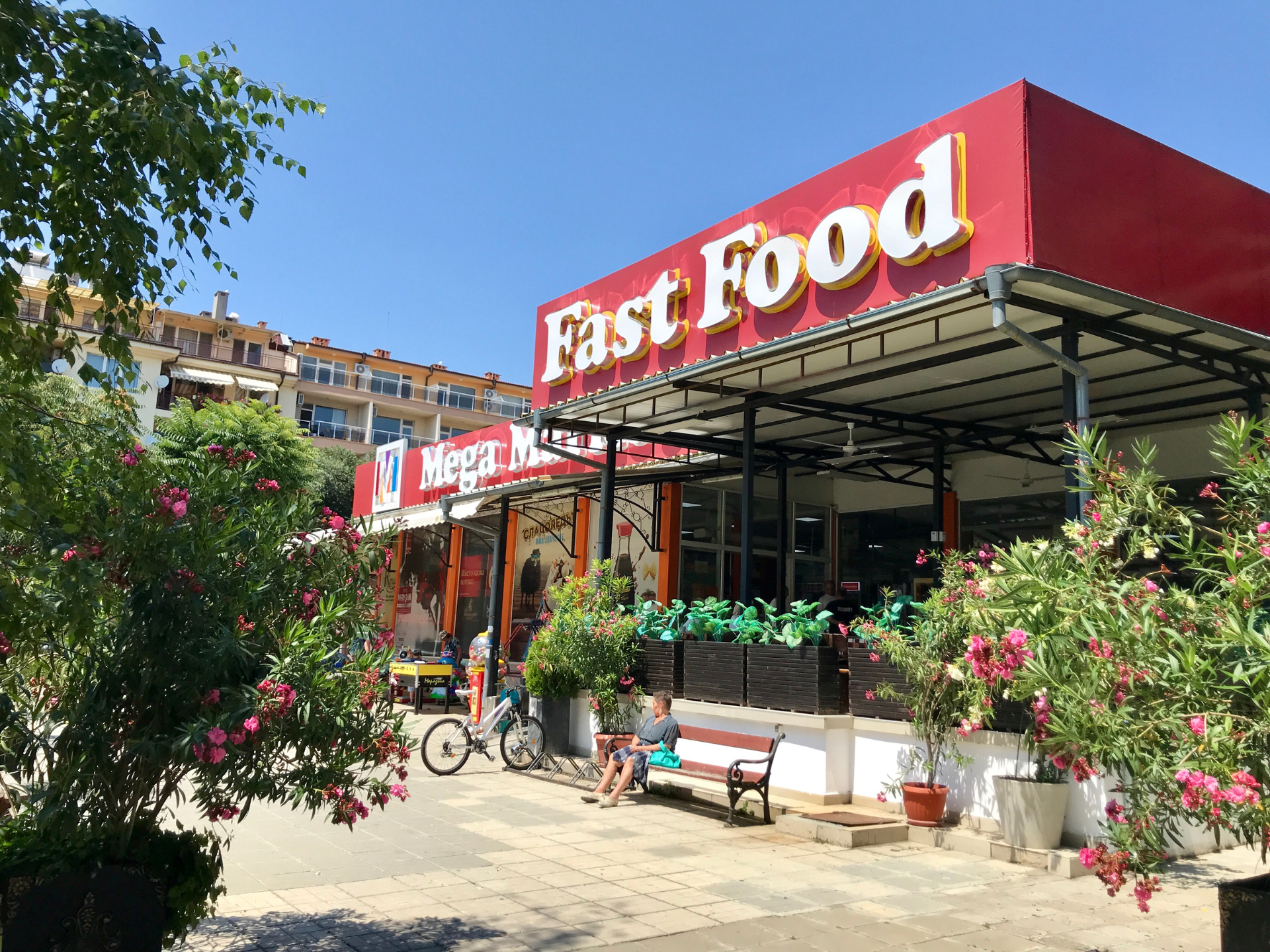 An outdoor view of a "Fast Food" restaurant and "Mega Market" storefront under a bright blue sky.