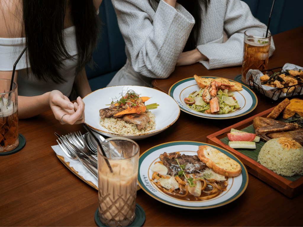 Photo of two people at a table in a restaurant, there are 4 plates on the table with food and an iced coffee