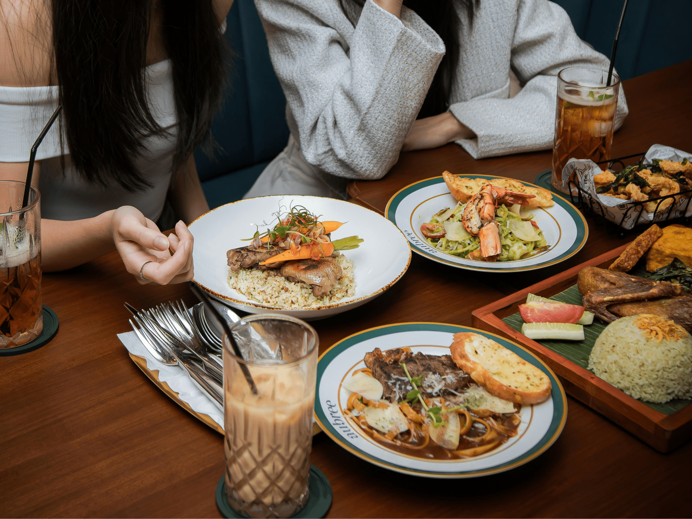 Photo of two people at a table in a restaurant, there are 4 plates on the table with food and an iced coffee